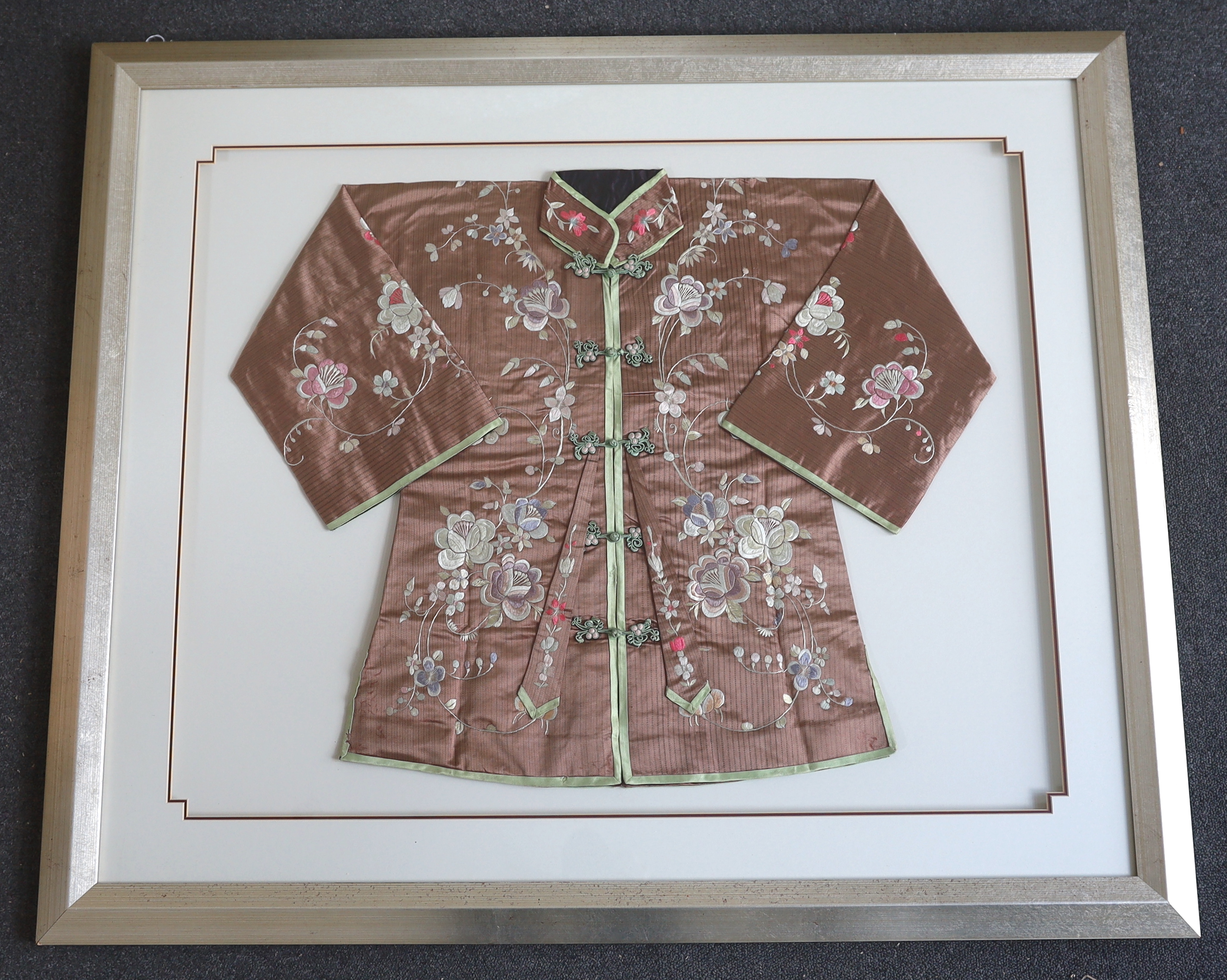 An early 20th century Chinese brown silk robe, with pastel multi-coloured all over embroidered flowers, framed and double mounted, measured as mounted: 75cm wide, 61cm high